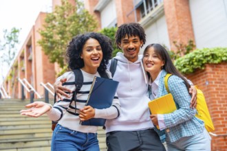 Low angle view portrait of three happy students posing smiling at camera in the campus
