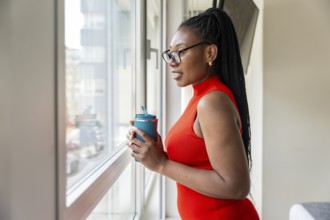 Black businesswoman enjoying a moment of peace while drinking from her travel mug and looking out
