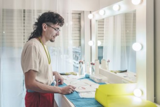 Young male make-up artist carefully reviewing face charts, preparing for diverse clientele in a