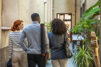Rear view of three diverse architects arriving at the coworking office carrying a drawing tube and