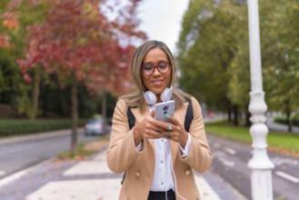 Frontal portrait of a happy distracted latin woman using phone walking along the street