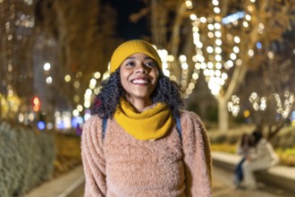 Portrait of a young woman wearing winter clothes, enjoying christmas lights in a decorated city at