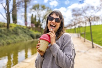 Carefree young woman enjoying a refreshing drink on a sunny day in a park, embodying a sense of joy