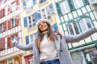 Low angle view photo of a happy stylish woman raising arms in the middle of street while visiting a