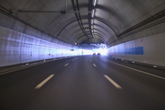 Modern, well-lit motorway tunnel with blue illuminated walls and a clear asphalt road, Switzerland,