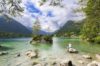 Hintersee with crystal clear water and mountains in the background, a woman sits on a rock and