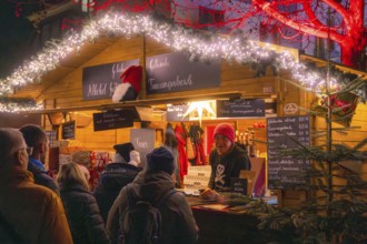 People standing at a cosy illuminated stall at a Christmas market at night, Christmas market