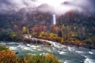 Waterfall with river Verzasca surrounded by autumn coloured deciduous trees, rainy and foggy