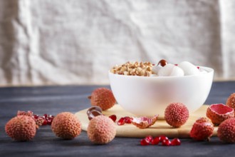 Greek yogurt with lychee, pomegranate seeds and granola in a white plate on a black wooden