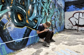 Ten-year-old boy playing with his Nintendo in front of a graffiti wall, football pitch, Germany,