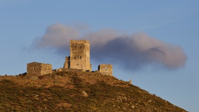 Sunset colours the clouds over the imposing ruins of a fortress on a mountain, residential tower on