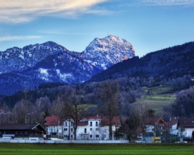 Idyllic village view with snow-covered Mount Wendelstein in the background and a green meadow under