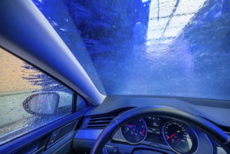 Car in an automatic car wash, car wash tunnel, cleaning foam is sprayed on, rotating brushes clean