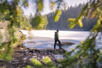 Man photographed through branches at the frozen lake, surrounded by forest and rocks, Glaswaldsee,