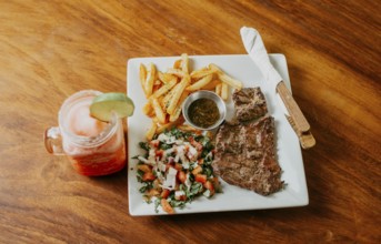 Plate of skirt steak with french fries and drink served on wooden table. Delicious homemade steak