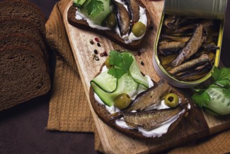 Sandwiches, black bread with sprats, cream cheese, cucumbers, on a cutting board, top view,