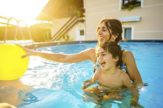 Happy mother and son laughing and playing with a yellow inflatable ball in a home swimming pool