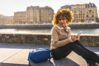 Side view with copy space of a latin beauty woman using phone sitting next to the river at city