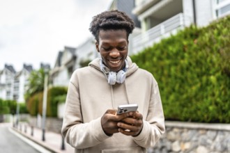 Confident african young man smiling while using phone standing in a residential street
