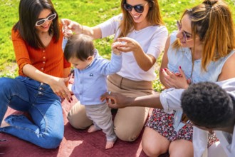 Group of happy multi ethnic friends having fun with a baby learning to walk during a picnic in a