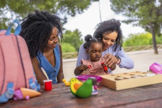 African grandmother and mother playing with girl in a park using toys sitting in a picnic table