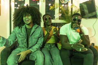 Three young multiracial people sitting on the sofa enjoying karaoke together at night