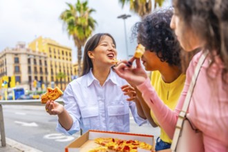 Three multiracial female friends chatting and eating pizza sitting on street