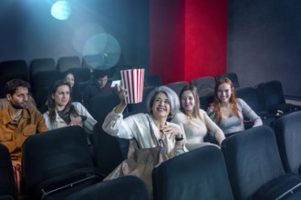 Mature woman enjoying a film in a movie theater, holding a popcorn bucket, surrounded by other