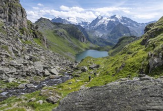 Hiker in front of mountain stream and mountain lake Lac de Louvie with glaciated summit of the