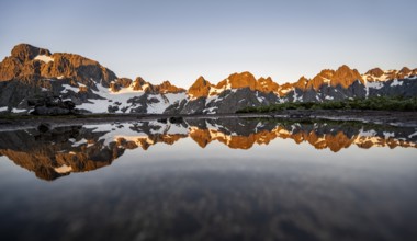 Rocky mountain peaks reflected in a small pond, mountain landscape with alpenglow at sunrise, at