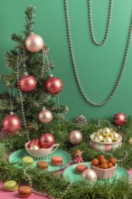 Table scene with small Christmas tree, pink baubles and macaroons, surrounded by green branches