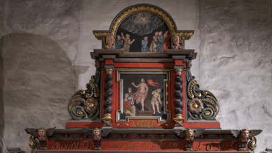 Close-up, richly decorated wooden altar in front of a stone wall, decorated with images of saints,
