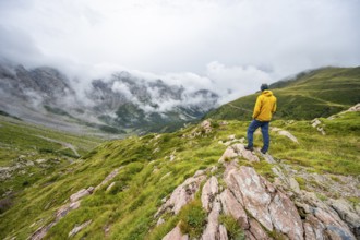 Mountaineer with yellow jacket looking at mountain landscape, cloudy rocky mountain peaks Wolayer