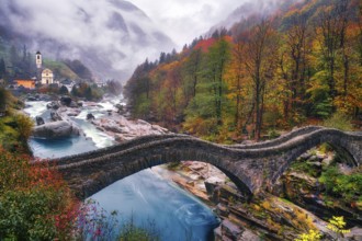Stone bridge Ponte dei Salti over river Verzasca on a rainy autumn day, behind it village view