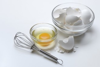 Egg whites and egg yolks in glass bowl and egg shells, whisk