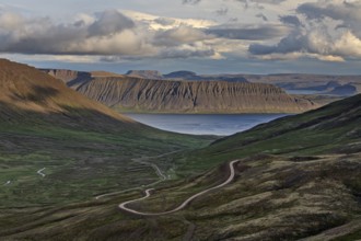 Winding gravel road, mountain road, fjord and mountains behind, cloudy mood, summer, Westfjords,