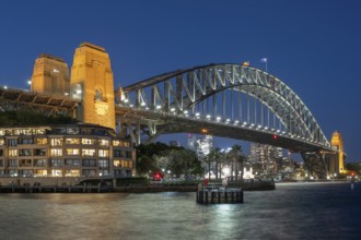 Sydney Harbour Bridge at night, illuminated at blue hour, with city lights in the background and