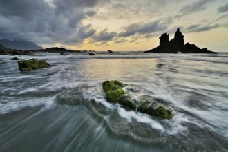 Dramatic cloudy atmosphere with rock formation at rising tide at sunset on the beach of Playa de