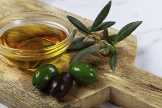 A glass bowl filled with rich olive oil sits on a wooden cutting board alongside fresh green and