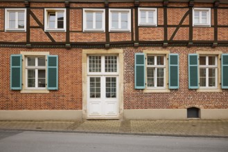 Facade of a half-timbered brick house with white windows, a mighty entrance door and blue-green