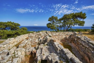 Ancient ruins with stone walls and views of the sea and trees under a blue sky, Kamiros,