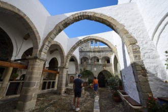 Historic monastery courtyard with stone arcades and bright white walls. Tourists explore the