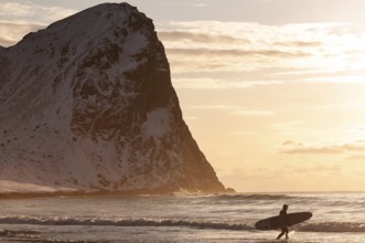 Surfer with surfboard under his arm on the beach of Unnstad, winter surfing, Lofoten Island