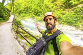 Tourist wearing an orange helmet and backpack takes a selfie while visiting vintgar gorge near bled