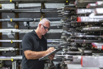 Side view photo of a mature caucasian man checking metal bars while doing inventory using a