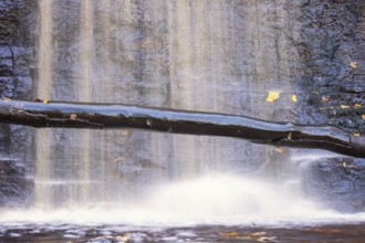 Waterfall on a rock face with a tree log