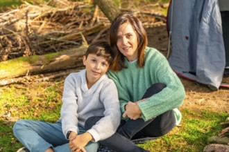 Caucasian mother and son smiling at camera sunbathing enjoying nature in the forest next to camping