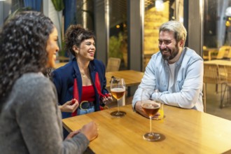 Multiracial friends enjoying night talking and drinking beer and cocktail in a bar terrace