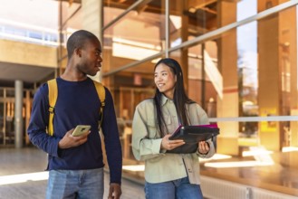 Multiracial chinese and african american students walking along the university talking distracted