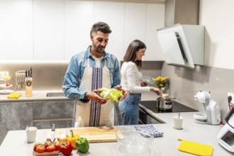Man holding lettuce and woman cooking in a modern kitchen, preparing a healthy meal together